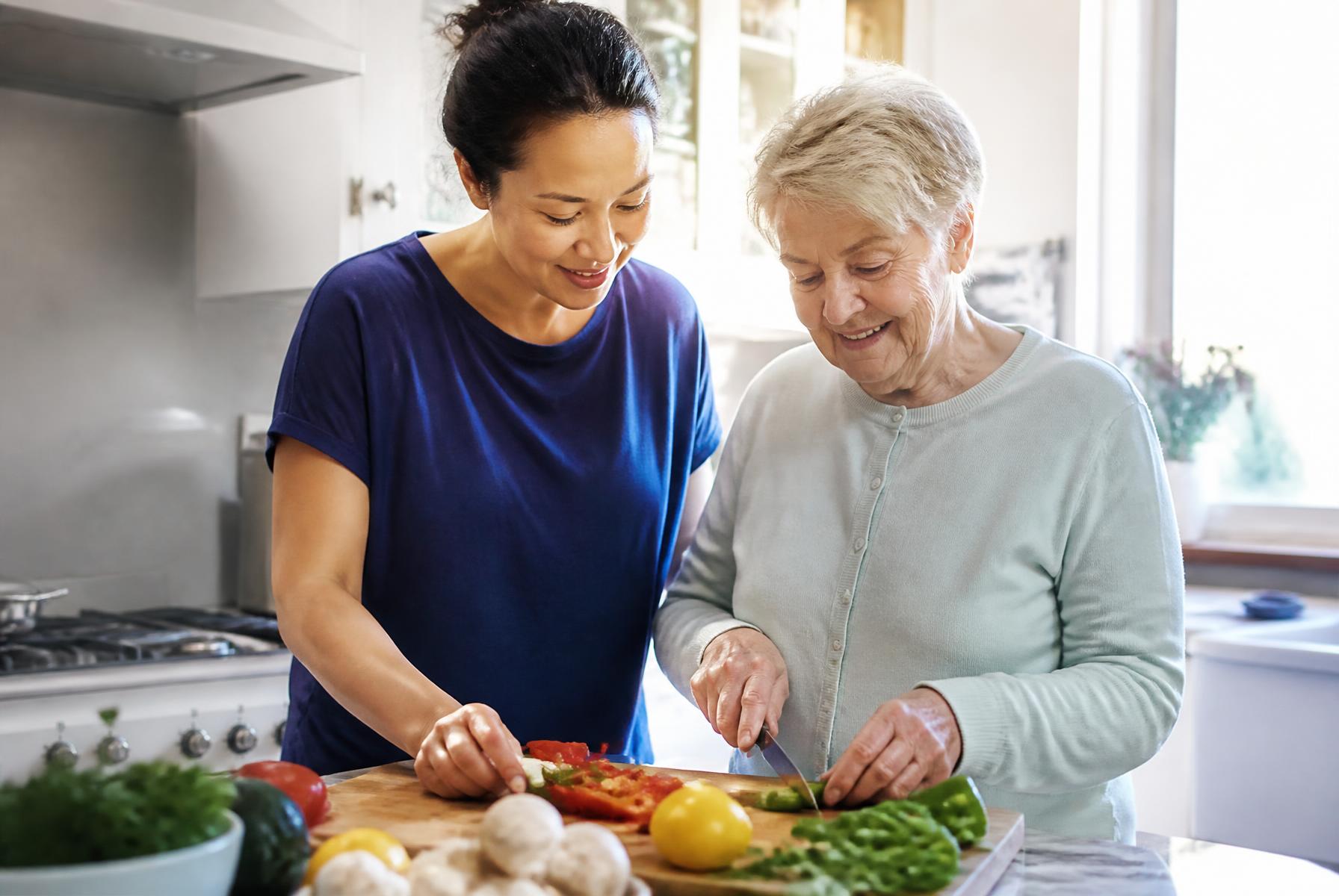 A care professional supporting an older woman to prepare vegetables in her kitchen