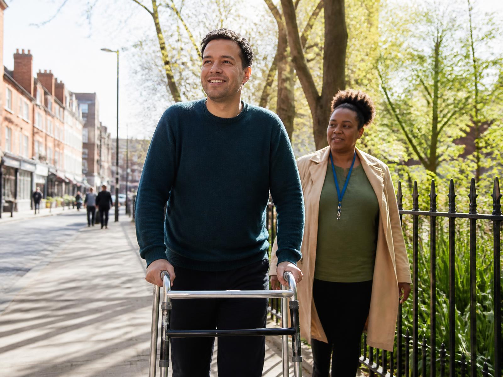 A working-age adult using a walking frame enjoying his local high street with a care worker nearby